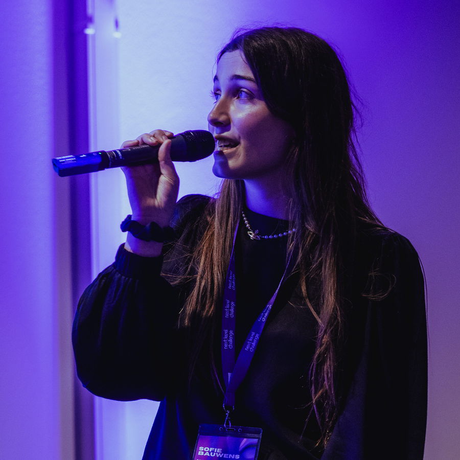 A participant presenting with a microphone under purple stage lighting